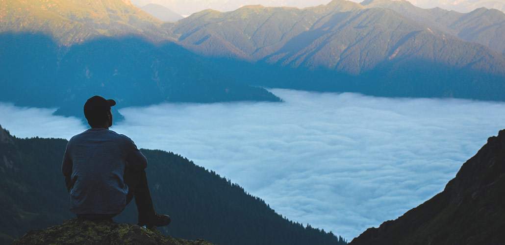 man sitting on mountain overlooking view of water and ridges