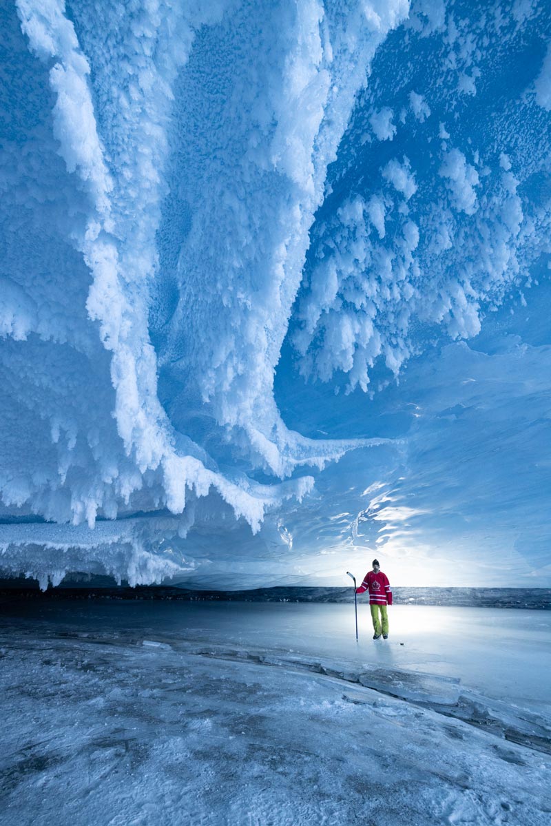 A man with a hockey stick and skates stands outdoors on ice