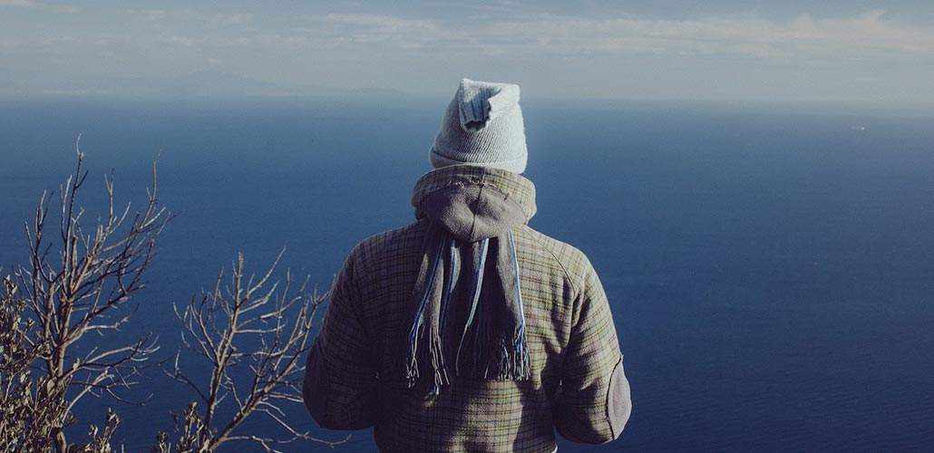 Man dressed in winter clothing staring out at large body of water