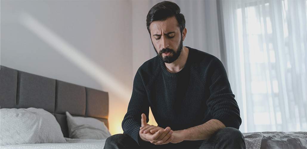 Picture of a man sitting on the edge of a bed, looking down